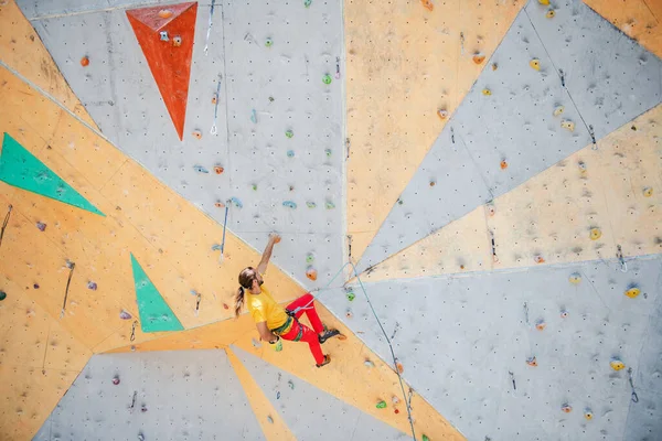 Genç ve formda bir adam dışarıda dağ tırmanışı yapıyor. Duvara tırmanan adam.