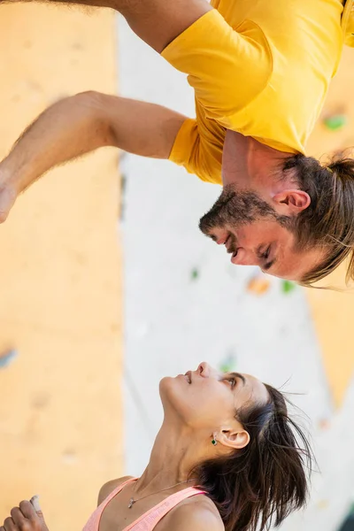 Man and woman on the background of an artificial climbing wall. The man hangs upside down at the level of the girl\'s head.