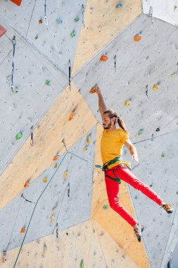 Bir adam tırmanma duvarında yüksek bir irtifada asılı dururken tek eliyle kendini tutar..