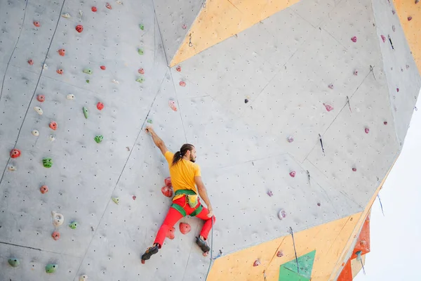 A man climbs up an artificial wall at a climbing wall. Bottom view.