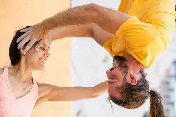 Man and woman on the background of an artificial climbing wall. The man hangs upside down at the level of the girl\'s head.