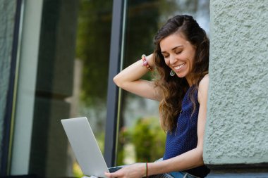 Young attractive woman with laptop sits on the windowsill outdoors. The girl straightens her hair with her hand.