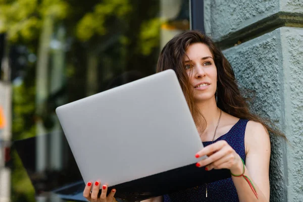 Young attractive woman with laptop sits on the windowsill outdoors. Huge window, showcase in the background.