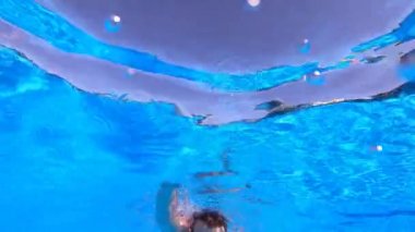 Handsome young man with a beard swims underwater. Bottom view. A man floats above the camera.