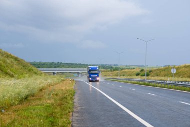 Big blue truck with roof spoiler transporting commercial cargo in semi trailer running on the evening wet glossy slippery road with raining weather