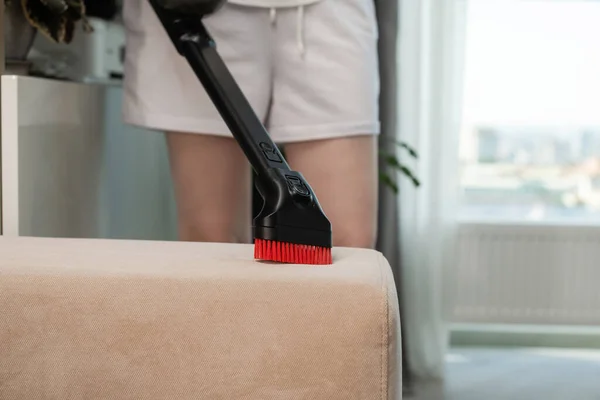 Woman vacuuming sofa. Sofa cleaning with vacuum cleaner. Home cleaning background. Dust cleaning in the house.