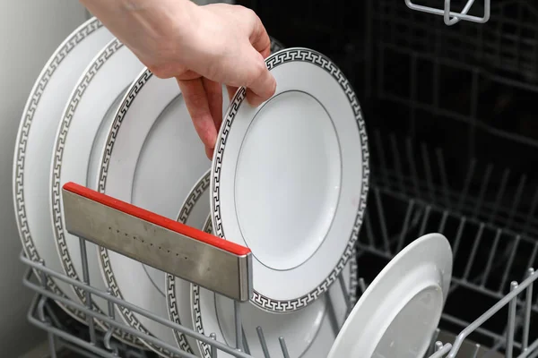 The female hand takes out a clean plate from the dishwasher. Clean dishes in the dishwasher close-up. Top view.