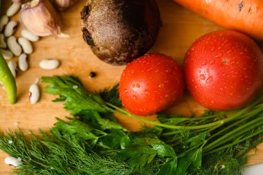 Close-up of tomatoes with various vegetables for cooking borscht on a wooden board in the kitchen. Top view.