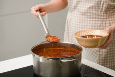 A woman pours freshly prepared Ukrainian borscht into a traditional earthenware bowl.
