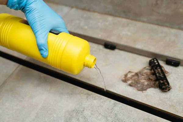 Woman using liquid drain cleaners to clean shower drain, close-up.
