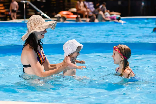 母はスイミングプールの水で2人の子供の娘と遊ぶ ホテルリゾートで幸せな家族の夏休み — ストック写真