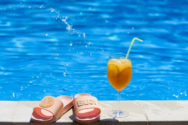 Summer vibes with citrus fresh ice cocktail with straw, swimming pool and beach flip flops shoes, happy chill and leisure, vacation background