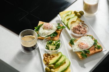 Kızarmış yumurtalı tost, maydanoz, dilimlenmiş avokado, beyaz tabakta tereyağı. Sabah kahvaltısı. Üst görünüm.