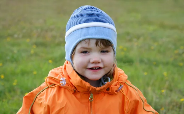 Happy little beautiful girl wearing orange jacket smiling on gre — Stock Photo, Image