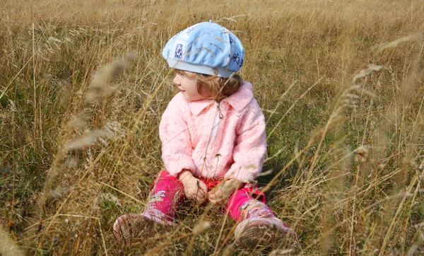 Little beautiful girl sitting in dry grass on field at summer — Stock fotografie