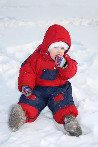 Küçük kız sıcak tulum giyen kar üzerinde oturur ve kara yiyor — Stok fotoğraf