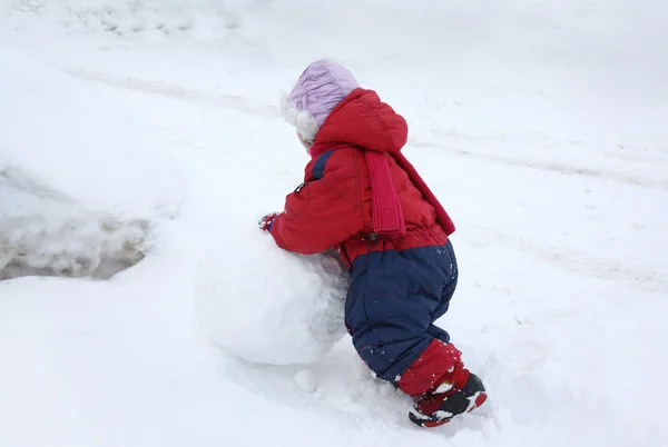 Achterkant meisje is dragen van warme jumpsuit rolling grote snowbal — Stockfoto