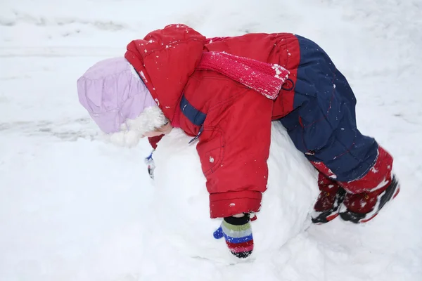 Liten flicka klädd i varma jumpsuit ligger på stor snöboll — Stockfoto