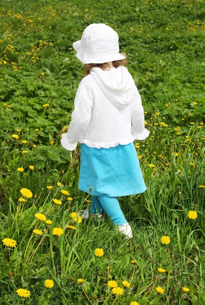 Back of little girl wearing white blouse walking on green field — Stock Photo, Image