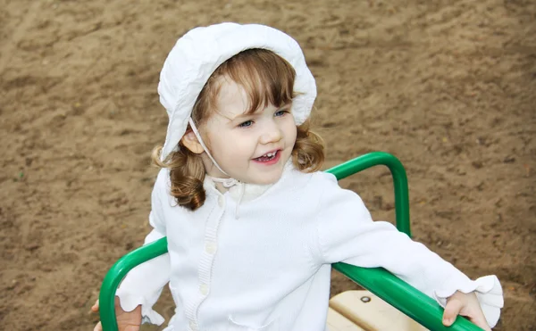 Happy cute girl wearing white panama rides on small carousel at — Stock Photo, Image