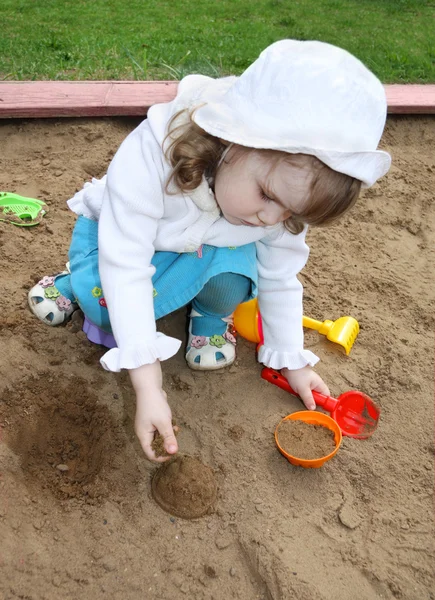 Little cute girl wearing white panama plays in sandbox — Stock Photo, Image