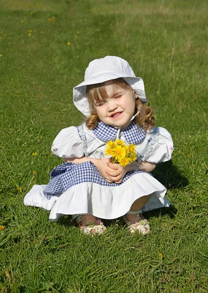 Beautiful little girl wearing dress with yellow dandelions sits — Stock Photo, Image