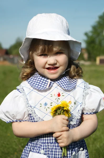 Bella bambina che indossa vestito tiene denti di leone gialli e — Foto Stock