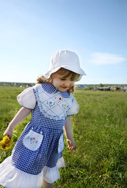 Happy little girl wearing dress and white panama walks on green — Stock Photo, Image