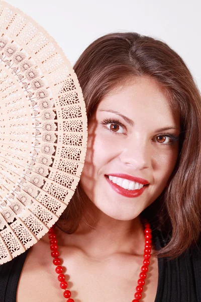 Beautiful smiling girl peeks out from behind fan and looks at ca — Stock Photo, Image