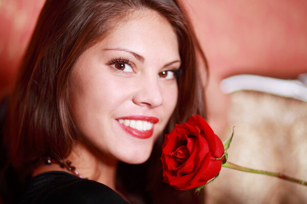 Beautiful happy girl holds red rose close to face and looks at c