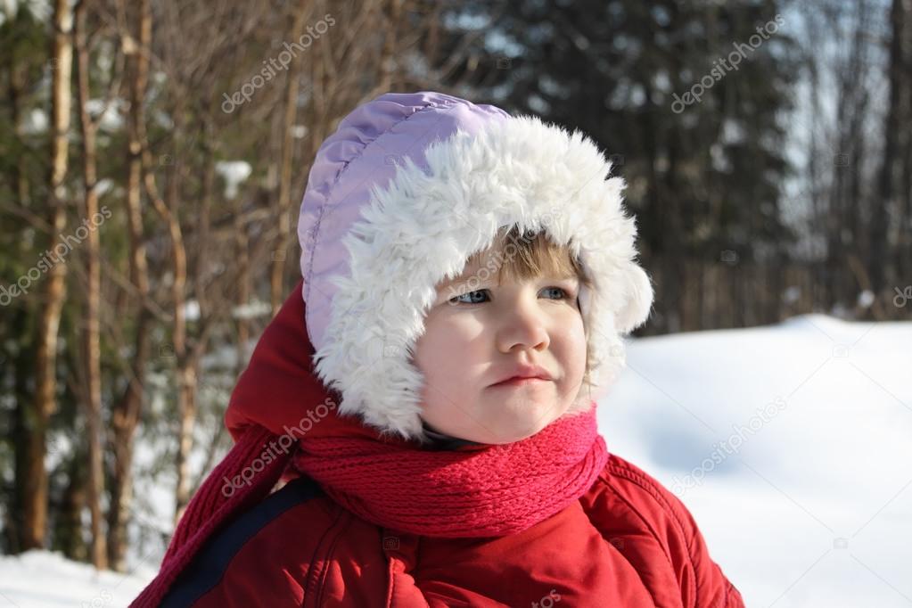Little sad girl stands in winter forest and looks into distance