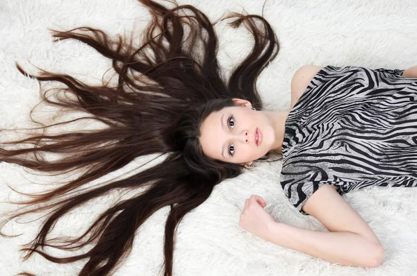 Junges Mädchen mit langen Haaren in gestreiftem Kleid liegt auf weißem Fu — Stockfoto