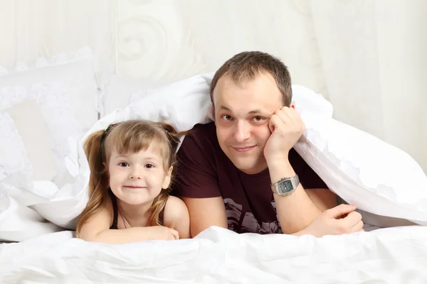 Little girl and her father look out from under blanket on bed an — Stock Photo, Image