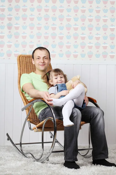 Feliz padre se sienta con su pequeña hija en mecedora en casa . — Foto de Stock