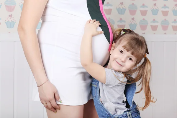 Happy little daughter touches belly of her pregnant mother at ho — Stock Photo, Image