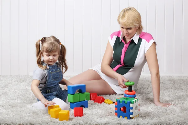 Happy little daughter and her pregnant mother play toys on carpe