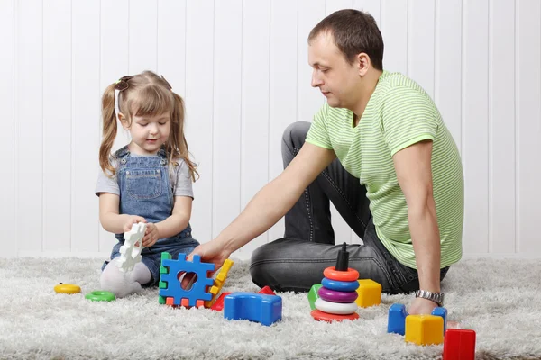 Felice piccola figlia e suo padre giocare giocattoli sul tappeto morbido a — Foto Stock