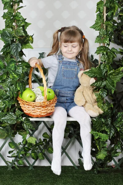 Happy little girl sits on swing under green ivy with teddy bear — Stock Photo, Image