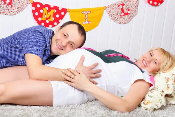 Glückliche schwangere Frau und Mann liegen auf Teppich und Mann hört zu — Stockfoto