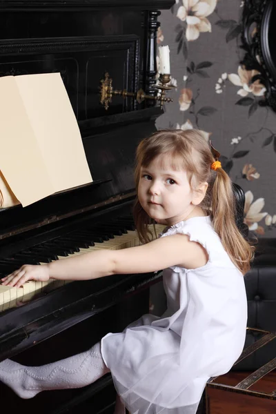 Piccola bella ragazza in abito bianco si siede al pianoforte nero con mu — Foto Stock