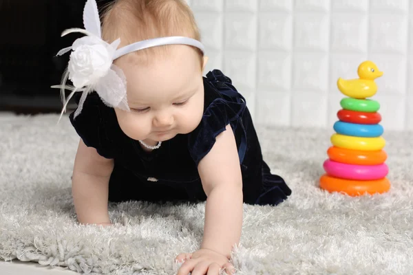 Little baby in dress creeps on grey soft carpet with colorful to — Stock Photo, Image