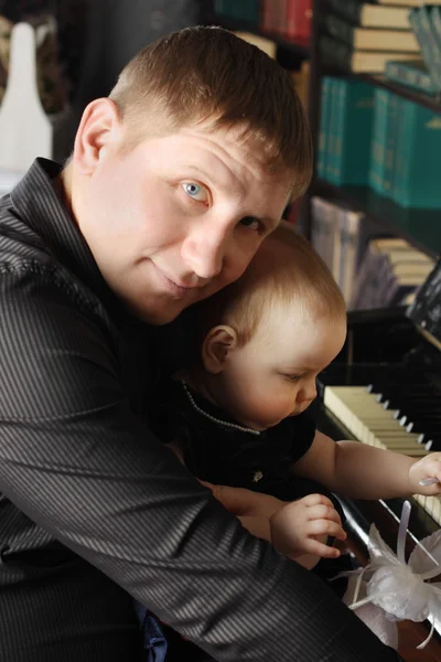 Cute baby sits at knees of her father and touches piano in room. — Stock Photo, Image