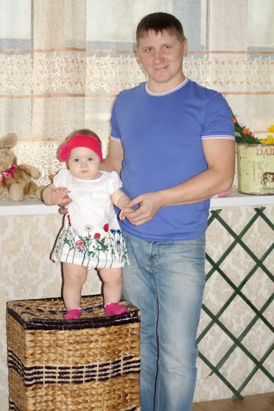 Kleines Baby steht auf großem Weidenkorb und ihr glücklicher Vater unterstützt sie — Stockfoto