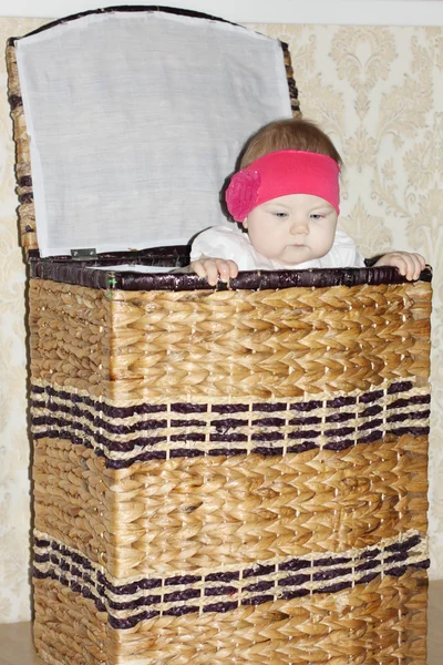 Little cute baby sits in big wicker basket and peeps out in room — Stock Photo, Image