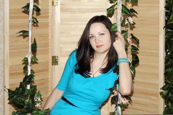 Piękna kobieta w niebieski siedzi na huśtawka porośnięte zielony bluszcz. — Zdjęcie stockowe
