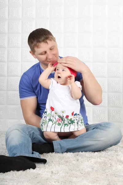 Feliz padre joven en jeans y pequeño bebé sentarse en alfombra suave . — Foto de Stock