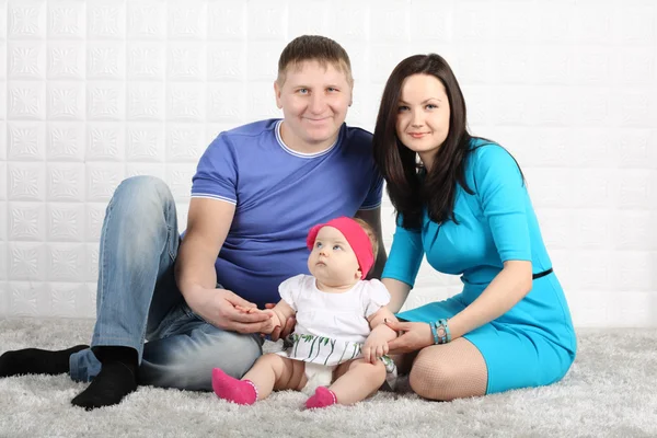 Happy young father, mother and baby sit on soft grey carpet. — Stock Photo, Image