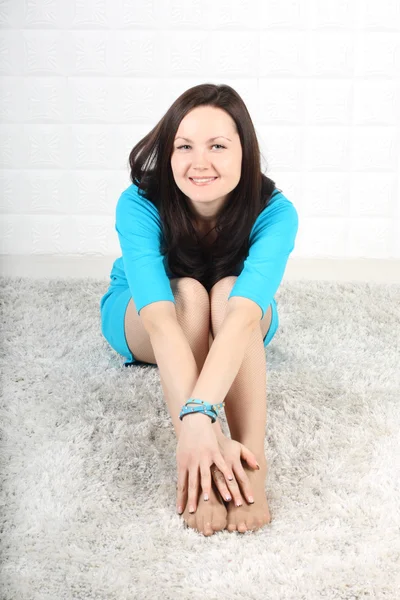 Mulher sorridente em vestido azul senta-se no tapete macio e olha para cam — Fotografia de Stock