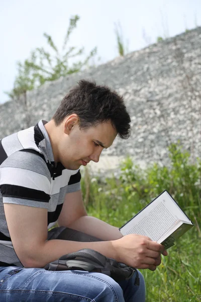 Young brunet man in jeans intently reads book outdoor at summer — Stock Photo, Image