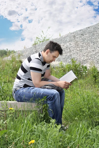 Giovane uomo in jeans legge intensamente libro all'aperto al giorno d'estate . — Foto Stock